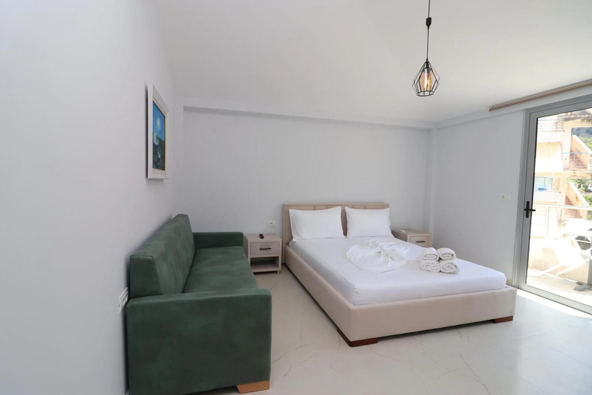 Bedroom with a wide bed, a green sofa and a sliding door onto a balcony above the bay