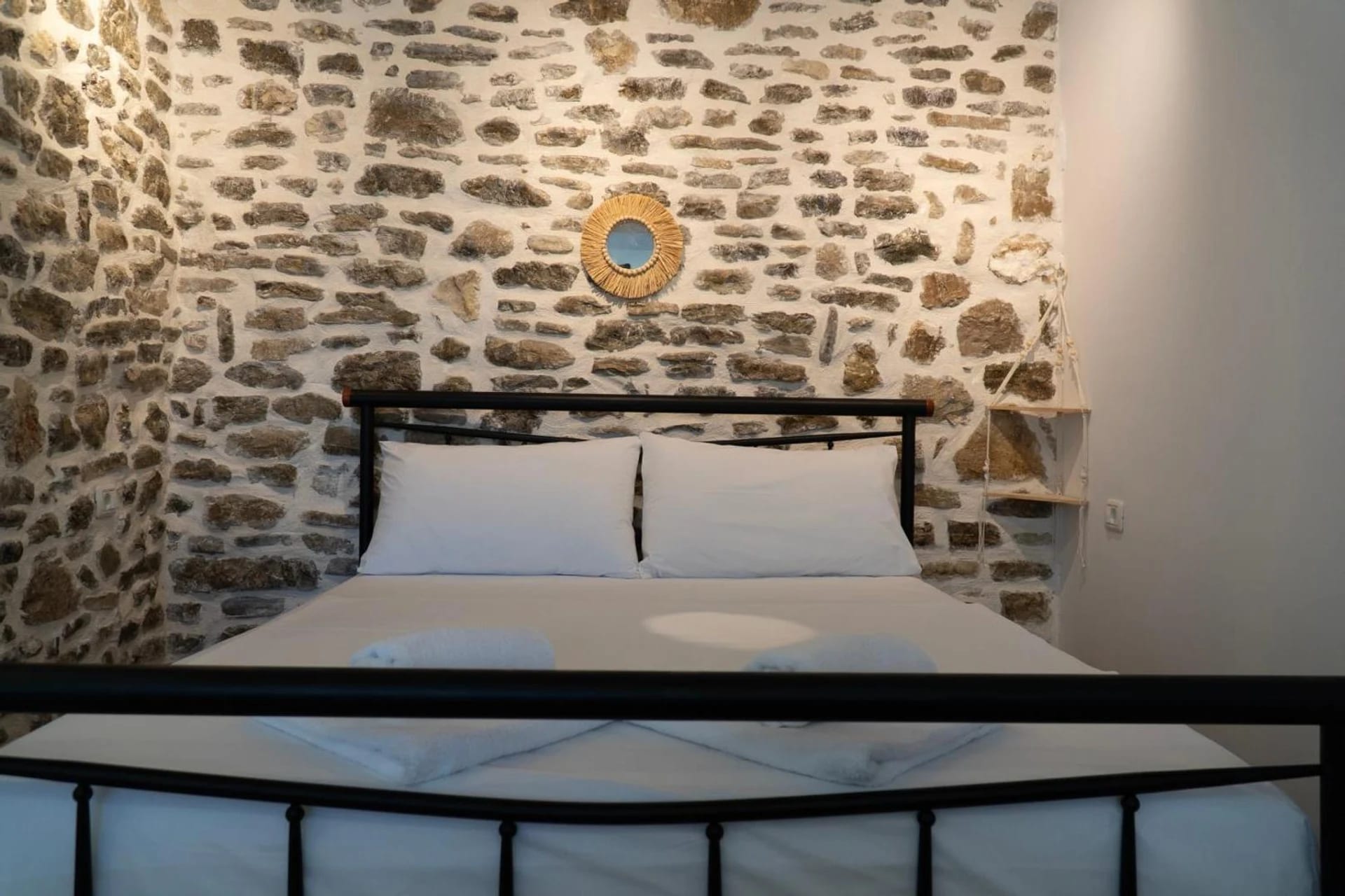 Double room with a black iron bed against an exposed stone wall and a pale wood floor