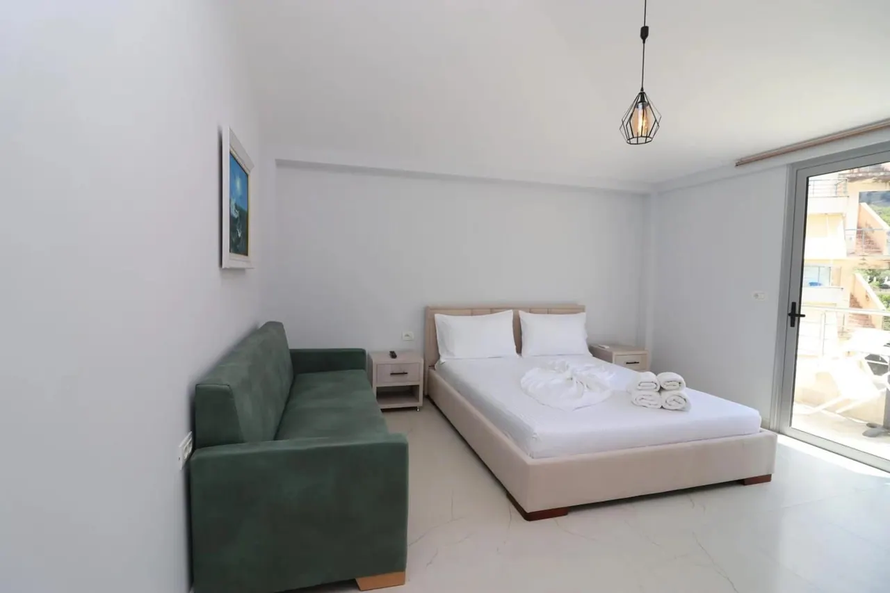 Bedroom with a wide bed, a green sofa and a sliding door onto a balcony above the bay
