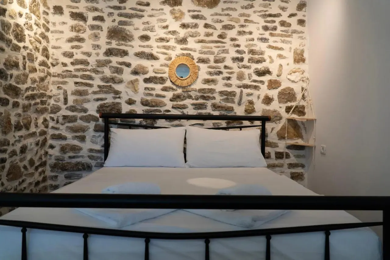 Double room with a black iron bed against an exposed stone wall and a pale wood floor
